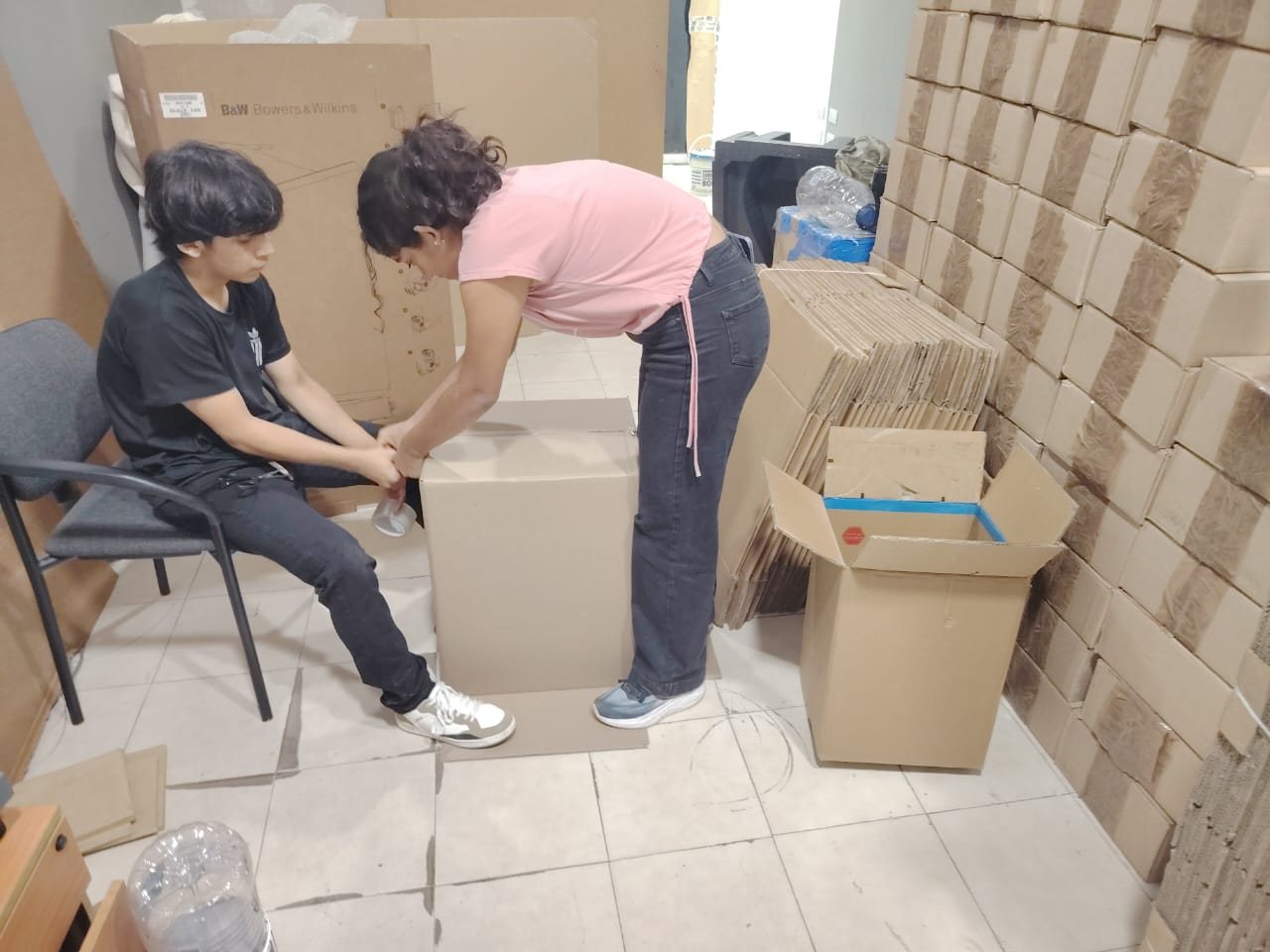 Dos jóvenes de la familia armando y cerrando una caja de cartón en el almacén de GJG