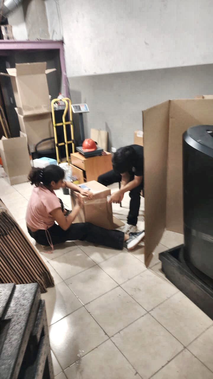 Los dos jóvenes sentados en el suelo del almacén, sellando una caja con cinta